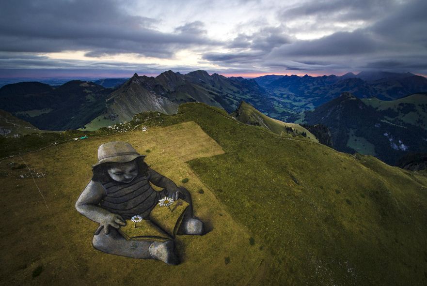 Gigantesca obra de una niña que lee un libro fue pintada sobre una montaña