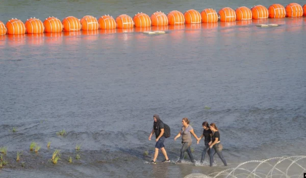 Migrantes caminan entre alambre de concertina y una serie de boyas colocadas en el agua a lo largo de la frontera de Río Grande con México para evitar la entrada de inmigrantes ilegales a EEUU en Eagle Pass, EEUU, el 16 de julio de 2023.