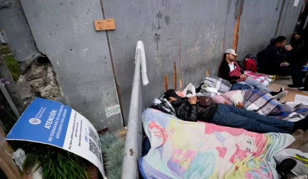 Personas que esperan para solicitar asilo duermen frente a un letrero de la aplicación CBP One mientras acampan cerca de la entrada peatonal del puerto de entrada de San Isidro el 1 de junio de 2023, en Tijuana, México.