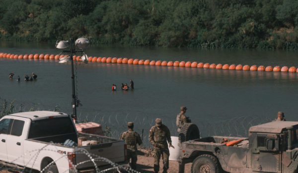 Migrantes en el Río Grande por una cadena de boyas destinadas a disuadir el cruce del río, en Eagle Pass. Jordan Vonderhaar/The New York Times