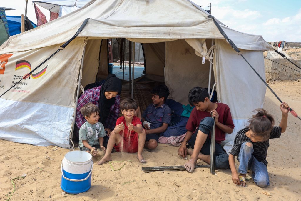 Randa Musleh, de 44 años, sentada con sus hijos en una tienda de campaña instalada en un campamento temporal en medio de un cementerio en Khan Yunis, al sur de la Franja de Gaza. (Foto de Omar AL-QATTAA / AFP)
