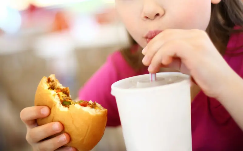Niña tomando malteada con una hamburguesa 