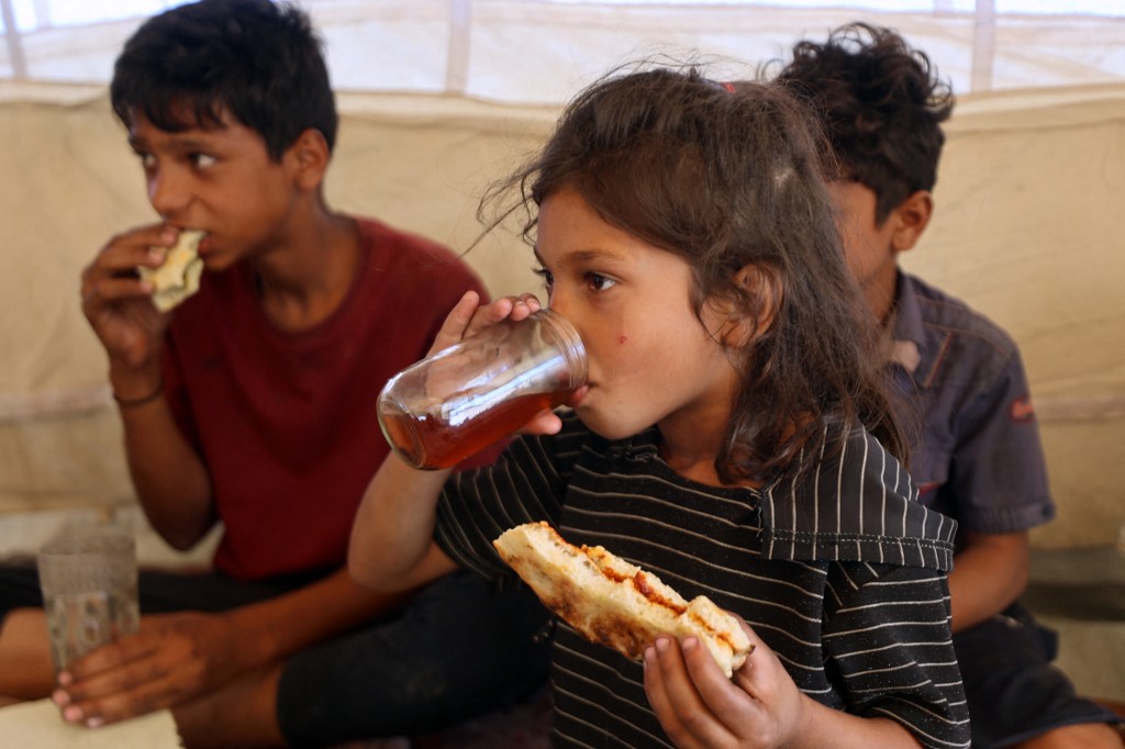 Niños palestinos comen algo en una tienda de campaña