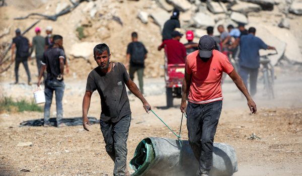Dos hombres tiran de un rollo de lona junto a otras personas que se dirigen a la ciudad de Gaza a través del llamado "corredor Netzarim" desde Nuseirat, en el centro de la Franja de Gaza. (Foto de Eyad BABA / AFP)