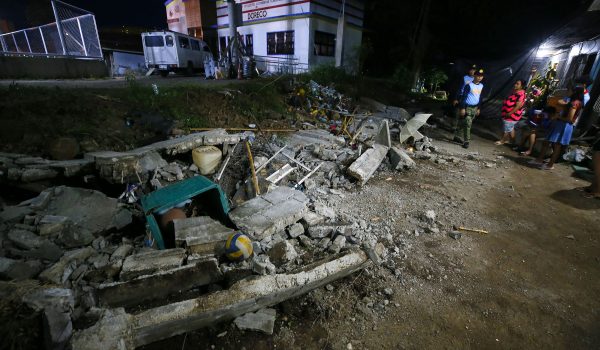 La policía permanece junto a los escombros de un muro derrumbado en la ciudad de Mati, provincia de Davao Oriental, en la isla sureña de Mindanao, tras un terremoto de magnitud 7,4. (Foto de Mark NAVALES / AFP)