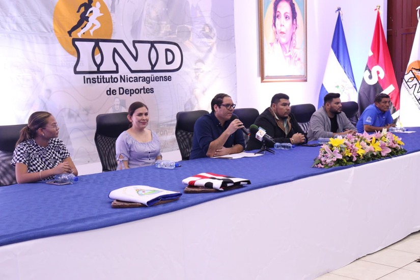 2025. Durante una actividad en el IND, Maurice Ortega ofrece declaraciones en un salón que exhibe el rostro de sus padres. La imagen destaca la de su madre y dictadora Rosario Murillo