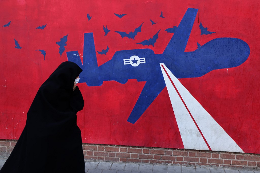 Esta fotografía, tomada el 1 de febrero de 2026, muestra a una mujer caminando junto a un mural que representa un dron estadounidense pintado en las paredes exteriores de la antigua embajada de Estados Unidos en Teherán, conocida popularmente como la "Guarida de Espías". Los murales y las pancartas han sido durante mucho tiempo un elemento distintivo del paisaje urbano iraní, particularmente en Teherán, donde estas pinturas en las plazas centrales a menudo reflejan el mensaje político y la postura de política exterior del Estado. ATTA KENARE / AFP