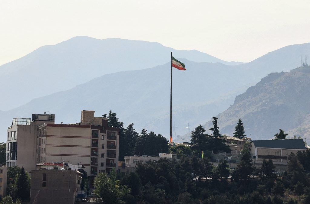 La bandera iraní ondea en un alto mástil sobre rascacielos en el norte de Teherán el 12 de mayo de 2026. El principal negociador iraní declaró ese mismo día que Washington debía aceptar el último plan de paz de Teherán o se enfrentaría al fracaso. FOTO: AFP/ATTA KENARE