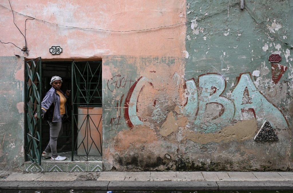 Una mujer se asoma por la puerta de su casa, junto a un muro con un grafiti que dice «CUBA», en una calle de La Habana, el 6 de mayo de 2026. La Habana acusó a Marco Rubio de «mentir» después de que el secretario de Estado estadounidense declarara el 6 de mayo de 2026 que Washington no había impuesto un embargo petrolero a Cuba y atribuyera la actual crisis energética de la isla a una mala gestión interna. (Foto de YAMIL LAGE / AFP)