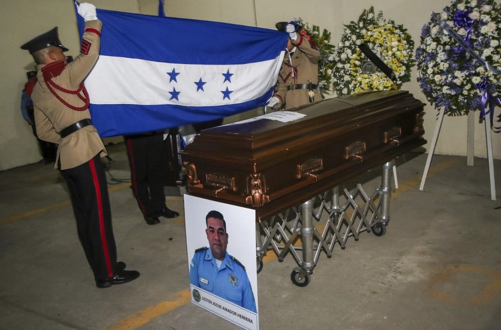 Guardias de honor de la policía despliegan una bandera nacional junto a uno de los féretros de cinco agentes de la policía antigang asesinados durante un tiroteo con presuntos miembros de un grupo de crimen organizado en Omoa, durante un velatorio celebrado en la sede de la Dirección Policial Anti Maras y Pandillas y Crimen Organizado (DIPAMCO) en Tegucigalpa, el 22 de mayo de 2026. Johny MAGALLANES / AFP