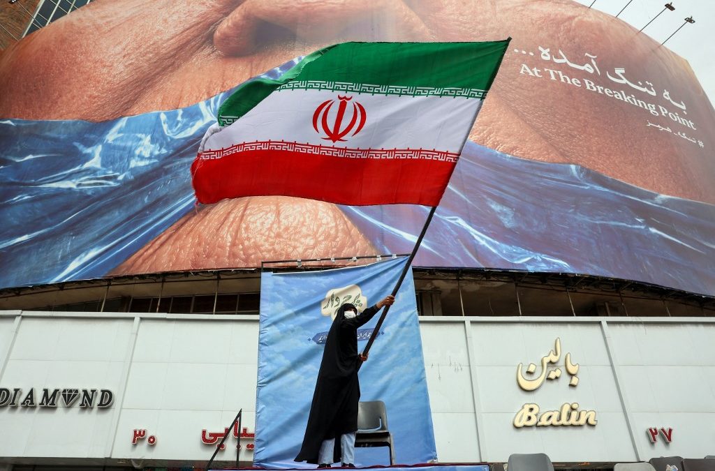 Una mujer ondea una bandera iraní frente a un cartel antiestadounidense que hace referencia al presidente de Estados Unidos, Donald Trump, y al Estrecho de Ormuz en la Plaza Valiasr de Tehran, el 5 de mayo de 2026. El principal negociador de Irán en las conversaciones con Estados Unidos advirtió el 5 de mayo que su país “ni siquiera ha comenzado” en su enfrentamiento por el Estrecho de Ormuz. (Foto de AFP)
