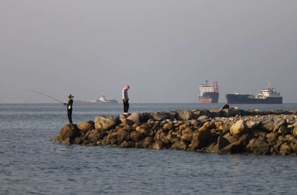 En esta fotografía, obtenida por la agencia de noticias iraní ISNA el 8 de junio de 2026, se ve a residentes pescando desde la costa mientras buques de carga y comerciales permanecen anclados en el estrecho de Ormuz, frente a Bandar Abbas, Irán. Amirhossein KHORGOOEI / ISNA / AFP