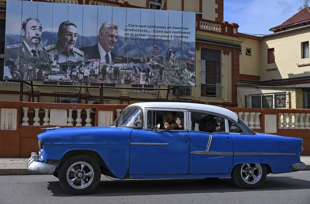Un automóvil estadounidense antiguo pasa frente a un cartel que muestra al fallecido líder cubano Fidel Castro (izq.), al expresidente de Cuba Raúl Castro (centro) y al actual presidente de Cuba, Miguel Díaz-Canel (der.), en La Habana, el 19 de junio de 2026. YAMIL LAGE / AFP
