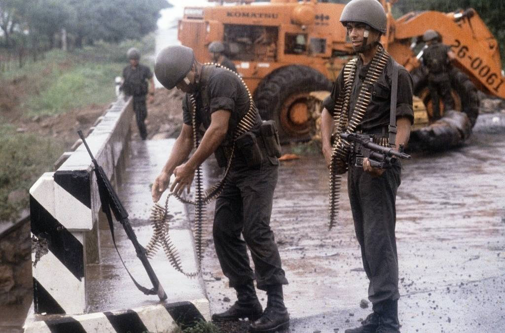 Un soldado de la Guardia Nacional se coloca una banda de tiros mientras otro observa atento sosteniendo una ametralladora FN MAG58 de fabricación Belga en un retén militar, en julio de 1979. LA PRENSA / MATTHEW NAYTHONS