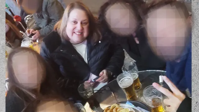 Una mujer de pelo rubio sonrie a la camara mientras toma un aperitivo con amigos.