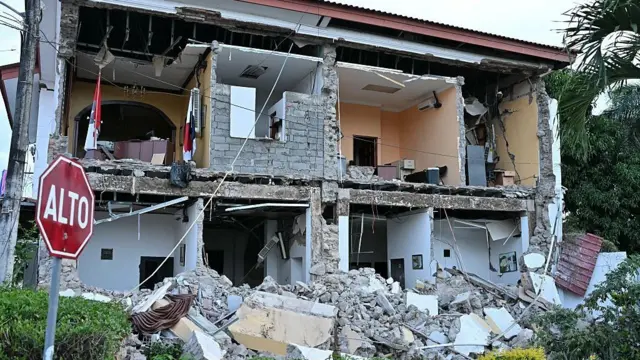Una casa semidestruida con un mensaje de Alto frente a ella.